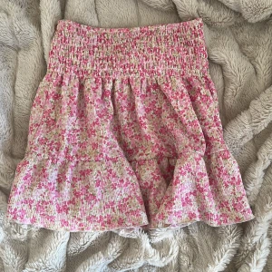 Blommig kortkjol/topp från Gina Tricot - Supersöt kortkjol eller topp  från Gina Tricot i blommigt mönster med rosa och gröna toner på vit botten. Jag andvände den som både kjol och tröja. Kjolen har smock i midjan och volang nertill. Perfekt för varma dagar! Nypriset är 279 kr, säljer för 120! Priset kan diskuteras. Skriv privat för Bilder på som kjol eller tröja! 