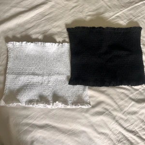 Svart och vit smockad tubtopp - Två smockade tubtoppar från H&M i svart och vitt. Båda har volangkant upptill och nedtill, och är gjorda i bomull med lite elastan för stretch. Perfekta att styla till jeans eller kjol för en enkel look. 