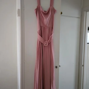 Ljusrosa långklänning med bälte - Säljer en elegant ljusrosa långklänning med breda axelband och matchande bälte i midjan. 