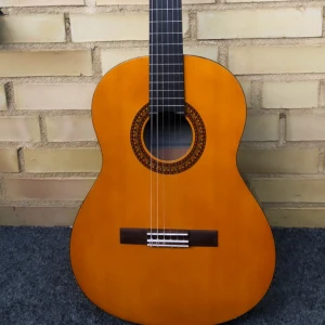 Gitarr i trä - Säljer en klassisk akustisk gitarr med naturlig träfärg och dekorativ rosett runt ljudhålet. Gitarren har sex nylonsträngar och mörkbrun baksida och hals. Perfekt för dig som vill börja spela eller behöver ett extra instrument.
