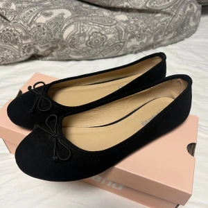 Svarta ballerinaskor med rosett - Säljer ett par klassiska svarta ballerinaskor. Skorna har rund tå, platt sula och en söt rosettdetalj framtill. Perfekta att matcha med både jeans och klänning. Säljs då dom e för små för mig, i mycket bra skick!