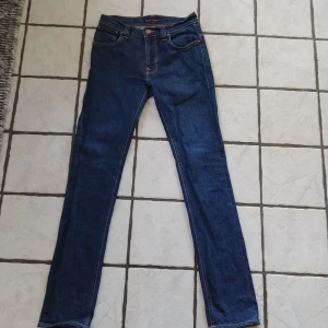 Mörkblå jeans från Nudie Jeans - Säljer ett par mörkblå jeans från Nudie Jeans med klassiska kontrastsömmar och broderade bakfickor. Modellen har normal passform och raka ben. Perfekta för dig som gillar stilrena och tidlösa jeans. Modell thinn finn. Storlek w29/l34