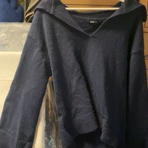 Mörkblå stickad tröja med krage från Gina Tricot - Mysig mörkblå stickad tröja från Gina Tricot med bred krage och långa ärmar. Perfekt för kyliga dagar och enkel att matcha med jeans eller kjol.