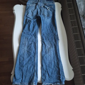 Blå bootcut jeans med slitningar - Säljer ett par blå bootcut jeans med slitningar på båda benen. Jeansen har klassisk femficksdesign och vida ben. Perfekta för dig som gillar en avslappnad och trendig stil.