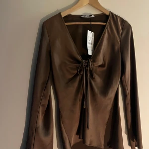 Brun satinblus med knytning från Zara - Säljer en brun långärmad satinblus från Zara med v-ringning och knytning framtill. Helt oanvänd med lappen kvar🤎