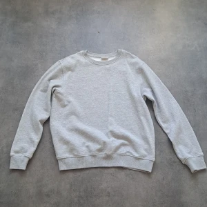 Ljusgrå sweatshirt från Kappahl - En basic ljusgrå sweatshirt från Kappahl med rund halsringning och långa ärmar. Tröjan har ribbade muddar vid ärmslut och nederkant. Perfekt för en enkel och stilren look. Pris kan diskuteras