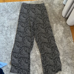 Svarta vida byxor med vitt prickigt mönster - Säljer ett par svarta byxor från BikBok med vitt prickigt mönster. Byxorna har en lös och bekväm passform med resår i midjan. Perfekta för en avslappnad och trendig stil. Byxorna är tunna och är perfekta för sommaren.