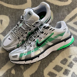 Nike P-6000 vit och grönt - Nike P-6000 sneakers i grått, vitt och grönt med svarta detaljer. Skorna har mesh- och syntetöverdel, snörning och en sportig design och Swoosh-logga. Perfekta för dig som gillar streetwear och sportig stil. Otroligt bra löparskor också! Aldrig använda utomhus. Original förpackning följer ej med. Pris går att diskutera vid snabb affär.