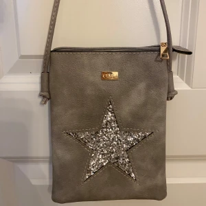 Grå axelväska med glittrig stjärna  - Säljer en grå axelväska med glittrig stjärna på, inga defekter förekommer på väskan🩷