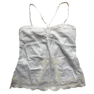 Vintage Vit broderad halterneck linnetopp  - Halterneck topp med gula broderade detaljer. Har gummi band längst med innerkanten för att inte glida ner! Strl 38 men passar oxå en S. Så S-M i storlek. 