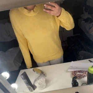 Gul stickad tröja med rund hals - Säljer en söt gul stickad tröja med rund hals och långa ärmar. Perfekt för att liva upp garderoben med en färgklick. Tröjan har en klassisk passform och ribbade muddar vid ärmslut och nederkant.