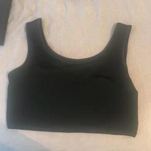 Svart croppad linnetopp - Säljer en enkel och stilren svart croppad linnetopp med breda axelband och rund halsringning. Perfekt att matcha med jeans eller kjol för en avslappnad look.