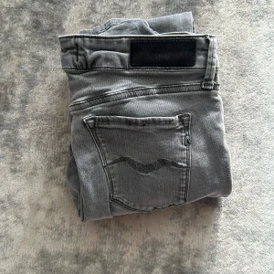 Grå slim jeans med svarta detaljer - Snygga grå jeans med slim passform och svarta detaljer på bakfickan samt svart patch vid linningen. Klassisk femficksmodell och raka ben. Perfekta till vardags för en stilren look.