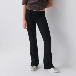 Svarta bootcut byxor med knappar - Snygga svarta bootcut kostymbyxor med låg midja och dubbla knappar i midjan. Byxorna har en stilren look och är tillverkade i ett stretchigt material som sitter bekvämt. Oanvända men ingen lapp. De har inte sömmar i fram som på första bilden🥰🥰