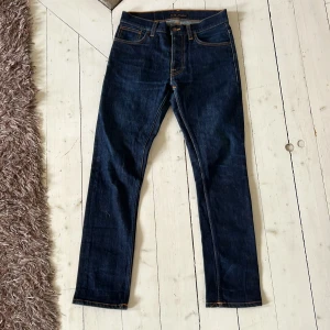 Mörkblå jeans från Nudie Jeans - Säljer ett par mörkblå jeans från Nudie Jeans med klassisk femficksdesign och orangea sömmar. Jeansen har rak passform och normal midja. Perfekta för dig som gillar stilrena och tidlösa jeans.