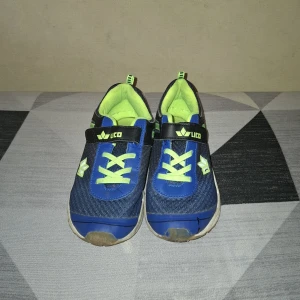 Blå sneakers med neongröna detaljer från Vico - Säljer ett par blå sneakers från Vico med neongröna detaljer och vita sulor. Skorna har snörning och kardborreband för enkel påtagning. Perfekta för träning eller vardag, med sportig look och bekväm passform.