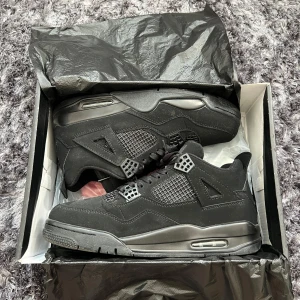 Nike Air Jordans 4 Black Cat - Pris kan diskuteras vid snabb affär! Säljer ett par nya helsvarta Nike Air Jordans 4 Retro med snygga detaljer och klassisk siluett. Skorna har snörning, meshpaneler på sidorna och synlig luftdämpning i sulan. Perfekta för dig som gillar streetwear och vill ha en ikonisk sneaker i garderoben. Obs, använd endast 1 gång! 