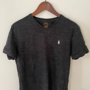 Mörkgrå t-shirt från Polo Ralph Lauren - Mörkgrå t-shirt från Polo Ralph Lauren. Skick 9/10 inga tecken på användning. Tillverkad i mjuk bomull, perfekt för en avslappnad stil.