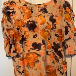 Mönstrad topp från Object - Säljer en färgstark topp från Object med abstrakt mönster i orange, beige och brunt. Toppen har trekvartsärm med rynkade detaljer och rund halsringning. 