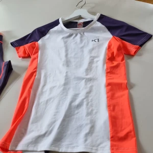 Tränings-set top/tights från Kari Traa - Sportig t-shirt från Kari Traa i vitt, lila och neonorange. T-shirten har korta ärmar och är tillverkad i ett lätt och funktionellt material som passar perfekt för träning. Snygg design med färgblock och logga på bröstet.