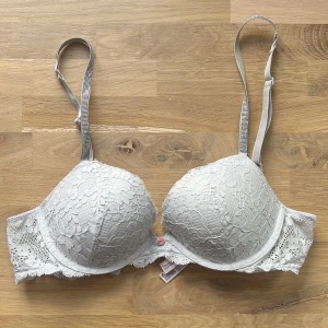 Ljus grå spets-bh, push up-bh från Victoria's Secret - Säljer en ljusgrå push up-bh från Victoria's Secret med vacker spets och justerbara axelband. Bh:n har bygel och vadering