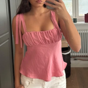 Rosa linnetopp med knytband från Zara - Supersöt rosa linnetopp från Zara med knytbara axelband och rynkad detalj vid bysten. Toppen har en lätt utsvängd passform och är perfekt för varma dagar. Aldrig använt 