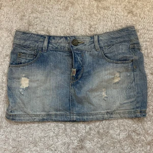 Blå jeanskjol från Pull&Bear - Säljer en blå lågmidjad jeanskjol från Pull&Bear med slitna detaljer och klassisk femficksdesign. Kjolen är köpt second hand i Köpenhamn. Perfekt för sommaren!