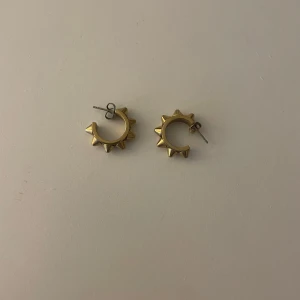 Guldiga örhängen med nitar - Coola guldiga örhängen i form av små hoops med markerade nitar runt om. Perfekta för dig som vill ha en edgy detalj till din stil. Säljs som par. Såklart tvättade innan och säljer pågrund av att de inte kommer till användning💕