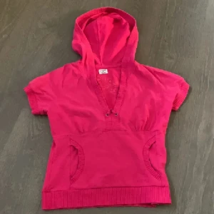 Rosa hoodie med kort ärm - Säljer en rosa hoodie från H&M med korta ärmar och magficka. Tröjan har djup v-ringning och ribbade detaljer vid ärmslut och nederkant. Perfekt för lager-på-lager och chill dagar. Vintage