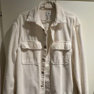 Vit overshirt från H&M - Säljer en vit overshirt i manchester från H&M. Skjortan har långa ärmar, knappar framtill och två stora bröstfickor med lock. Perfekt att styla lager på lager. Storlek S. Använder ej längre. Är i bra skick.