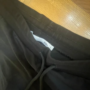 Svarta mjukisbyxor med dragsko - Svarta mjukisbyxor med rak passform och dragsko i midjan. Perfekta för en avslappnad stil och sköna att ha på sig. Byxorna har resår i midjan och är tillverkade i ett mjukt material.