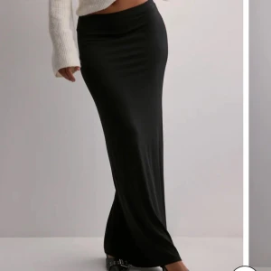 Svart långkjol i stretchigt material - Säljer en svart långkjol med tight passform och stilren look. Kjolen är gjord i ett stretchigt, mjukt material som sitter snyggt och följsamt längs kroppen. Perfekt att styla med en croppad topp eller stickad tröja.