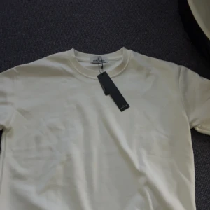 Vit långärmad tröja från Stone Island - Säljer en stilren vit långärmad tröja från Stone Island med klassisk logotyp-patch på ärmen. Tröjan har rund halsringning och är tillverkad i mjuk bomull. Perfekt för en clean och enkel look.