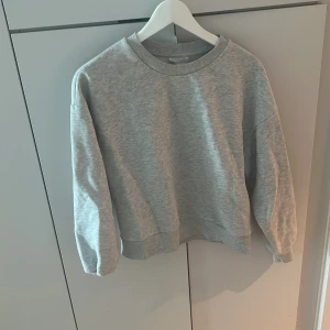 Grå sweatshirt - En klassisk grå sweatshirt med rund halsringning och långa ärmar. Tröjan har en enkel och stilren design, perfekt att matcha med jeans eller mjukisbyxor. Mjuk och bekväm. Från Gina tricot