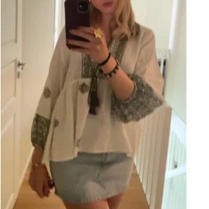 Vit blus med grönt mönster och knytband - Säljer en luftig vit blus med grönt mönster på ärmslut och runt halsen. Blusen har långa ärmar och dekorativa knytband framtill. Perfekt för dig som gillar bohemisk stil.