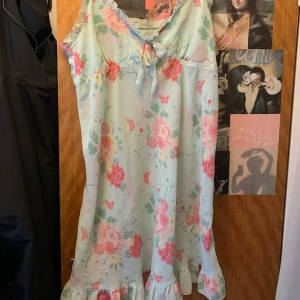 Blommig mintgrön klänning med volang - Söt mintgrön klänning med stora rosa blommor och volang nertill. Klänningen har knyt framtill vid bysten och är ärmlös, perfekt för varma dagar. Lätt och luftig modell som ger en romantisk känsla.