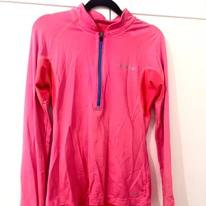 Rosa långärmad träningströja från SOC - Säljer en rosa långärmad träningströja med halv dragkedja framtill och diskret logga på bröstet. Perfekt för löpning eller gym. Materialet är syntetiskt och andas bra.