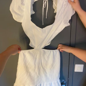 Vit omlottklänning med volang och öppen rygg - Superfin vit klänning med omlott-skärning, volangdetaljer och öppen rygg med knytband. Puffiga korta ärmar och lätt rynkad kjol. Perfekt för studenten eller midsommar!