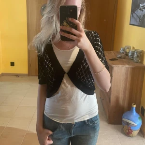 Svart bolerotopp i spets - Säljer en svart bolerotopp i spets med korta ärmar. Toppen är öppen framtill och har ett snyggt mönster. Funkar toppen över ett linne eller t-shirt. Har ett litet hål i ena axlen som knappt syns därför lågt pris.❤️