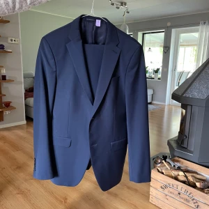 Mörkblå kostym från Turo - Säljer en stilren mörkblå kostym från Turo. Kavajen har klassisk passform med två knappar framtill, fickor med lock och snygga detaljer i fodret. Perfekt för formella tillfällen och student. Använd två gånger och den kommer kemtvättad.   Kavaj storlek: 48 kostymbyxorna storlek: 148