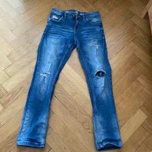 Blå slitna jeans med hål ,storlek 146 - Säljer ett par blå jeans med slitningar och hål på ena benet. Jeansen har klassisk femficksdesign och raka ben. Tillverkade i mer hållbar denim. Storlek 146.Vi kan diskutera priser.skriv till mig om du har frågor.