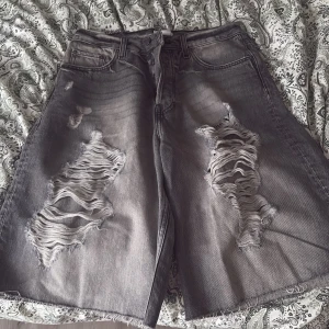 Grå slitna jorts från Weekday - Grå jeansshorts från Weekday med rejält slitna detaljer och råa kanter. Modellen är loose fit och har klassiska fem fickor samt knappgylf. Perfekta för en avslappnad stil. Köpte för 750🤗