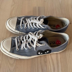 Grå Converse Play Comme des Garçons sneakers - Grå låga Converse Play Comme des Garçons sneakers med vit sula och tå, vita skosnören och det ikoniska hjärtloggan med ögon på sidan. Klassisk design med canvasmaterial och rund tå. Dm för frågor!