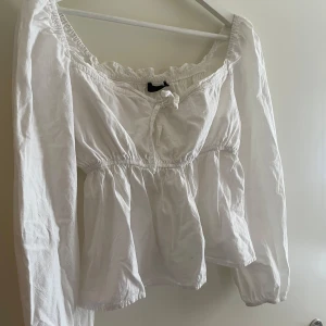 Vit blus med knyt och volang - Säljer en söt vit blus med långa ärmar och knyt framtill. Blusen har volangdetaljer vid halsringningen och ett luftigt matrial. Sitter så fint på. 