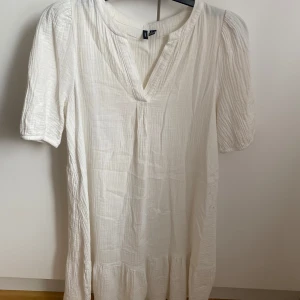 Vit klänning från Vero Moda - Säljer en luftig vit klänning från Vero Moda med korta ärmar och v-ringning. Klänningen har en avslappnad passform och är tillverkad i ett mjukt, lätt material som ger en skön känsla. Perfekt för varma dagar!