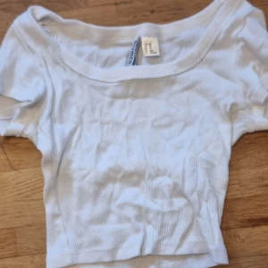 Vit ribbad croppad topp från H&M Divided - Säljer en vit ribbad croppad topp från H&M Divided. Toppen har korta ärmar och en rundad urringning. Perfekt att matcha med jeans eller kjol för en enkel och stilren look. Den är använd 1 gång men tråden har lossat i kanten ayna i de sista bilderna 