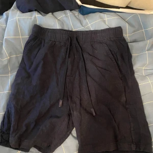 Mörkblå linneshorts från Zara med snörning - Säljer ett par mörkblå shorts från Zara med elastisk midja och snörning. Shortsen har två sidofickor och är tillverkade i linen som passar perfekt för sommardagar.
