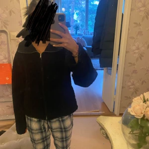 Svart teddyjacka med dragkedja - Mysig svart teddyjacka med dragkedja framtill och stor krage. Jackan har en avslappnad passform och är perfekt för kyligare dagar. Enkel och stilren design som passar till många outfits.