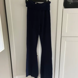 Mörkblå stickade byxor från Nelly - Mörkblå stickade byxor från Nelly med bred ribbad midja och utsvängda ben. Perfekta för en avslappnad och trendig look. Mjukt och bekvämt material som passar till många olika stilar. Finns en matchade tröja till