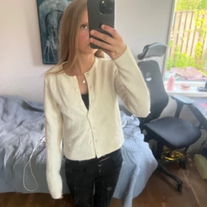 Vit kofta med rund hals - Säljer en enkel och stilren vit kofta med rund hals och knäppning framtill. Koftan har långa ärmar och är gjord i ett mjukt material som passar perfekt till lager-på-lager-stil.